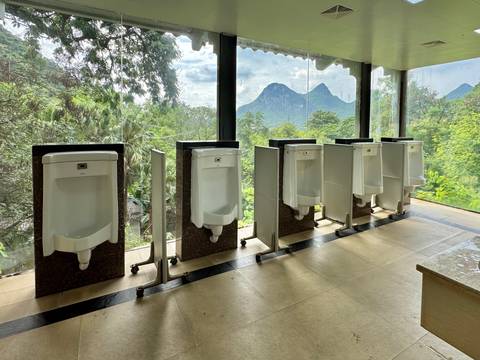 Row of spotless urinals facing a panoramic glass wall that looks onto green hills and karst peaks.