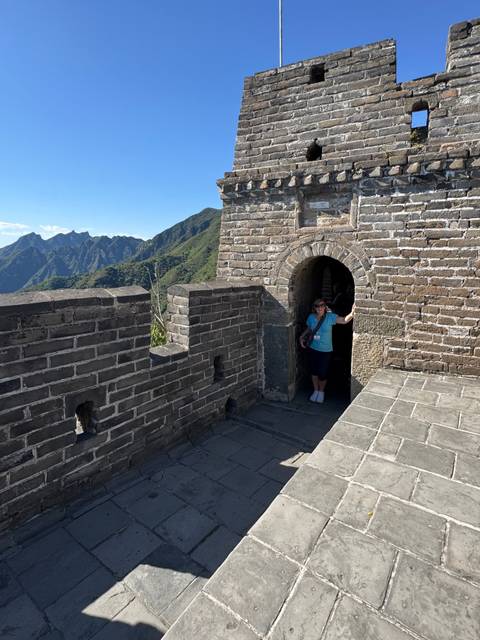Visitor emerges from an arched doorway on the Great Wall with rugged mountain scenery behind.