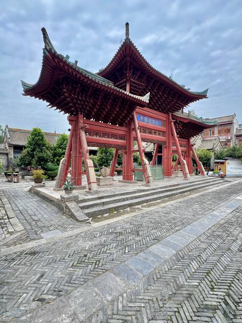 Traditional red wooden ceremonial gate in a quiet courtyard surrounded by potted plants and tiled roofs.