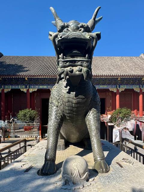 Massive bronze qilin statue standing guard before ornately painted palace halls.