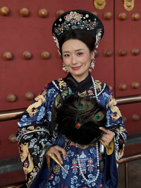Studio-style portrait of a woman in ornate Qing-era robes holding a peacock feather fan.