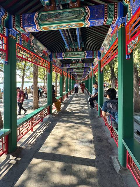 Long, colorfully painted covered walkway lined with green pillars and red lattices at the Summer Palace lakefront.