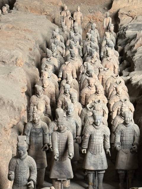 Close-up overhead view of rows of weathered Terracotta Warriors standing in excavation pits.