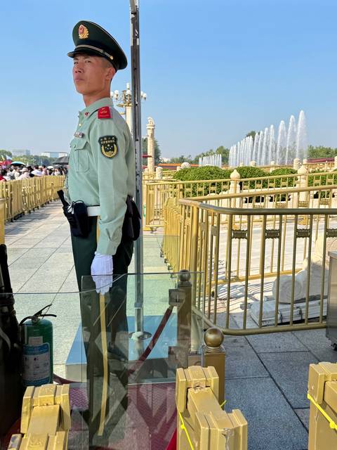 Uniformed Chinese guard standing beside gold railings and fountains at Tiananmen Square.