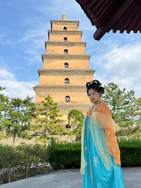 Woman in colorful Tang-style dress posing in front of the Giant Wild Goose Pagoda on a bright day.