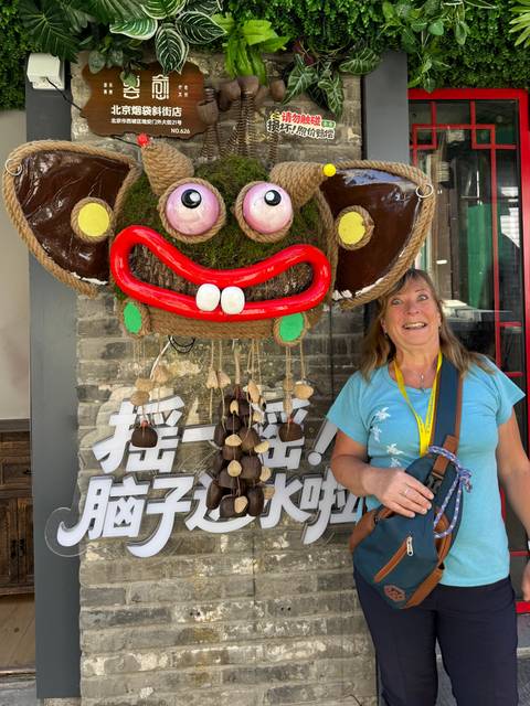 Tourist laughing beside a large colorful moss mask decoration mounted on a brick wall.