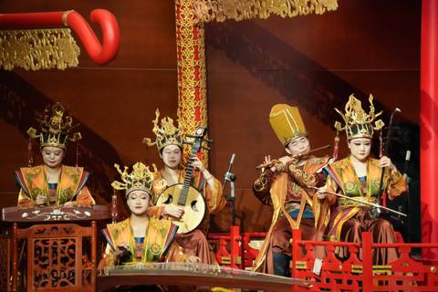 Traditional Chinese orchestra in ornate golden costumes performing on stage with classical instruments.