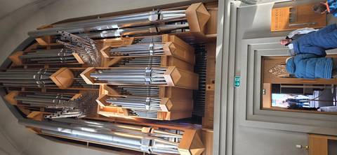Massive silver pipe organ inside a modern church with visitors standing below