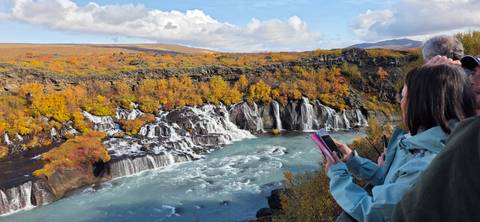 Visitors admire a wide turquoise waterfall framed by vivid autumn colors