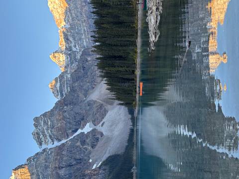 Calm alpine lake with a single orange canoe under glowing mountain peaks at golden hour