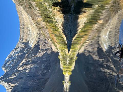 Crystal clear alpine lake perfectly mirroring steep rocky mountain walls under a blue sky