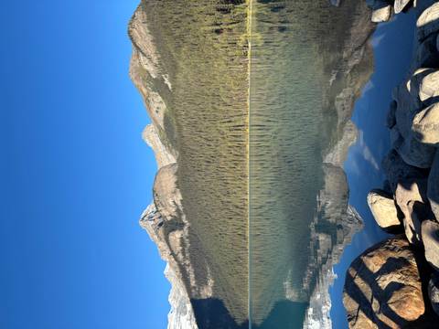 Wide tranquil lake with rocky shoreline and dense conifer forest beneath towering peaks