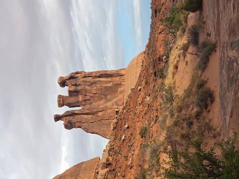 A towering trio of sandstone monoliths rises from the red desert floor beneath a pastel sky.