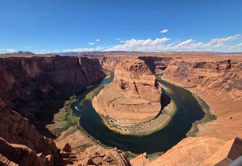 A sweeping view of Horseshoe Bend shows the emerald Colorado River looping around a sheer sandstone mesa beneath a bright sky.