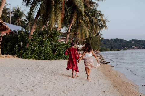 Two women holding hands while strolling along a tropical sand beach at dusk