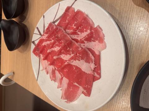 Plate of thinly sliced raw beef prepared for hot pot on a restaurant table.