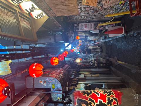 Narrow alleyway lined with tiny eateries and red lanterns, bustling with evening diners in Tokyo.