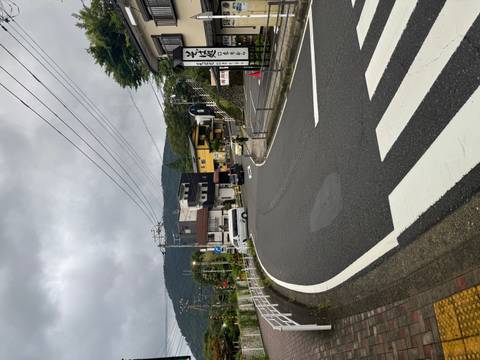 Quiet winding road through a small mountain town on a cloudy day with forested hills in the background.