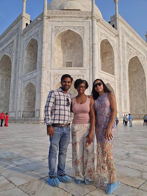 Three travelers pose in front of the intricately carved white marble walls of the Taj Mahal.
