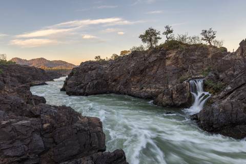 Powerful rapids surge through dark rocky canyon at sunset with distant hills aglow