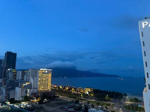 Evening city skyline with illuminated hotels beside a calm beach and darkening blue sky