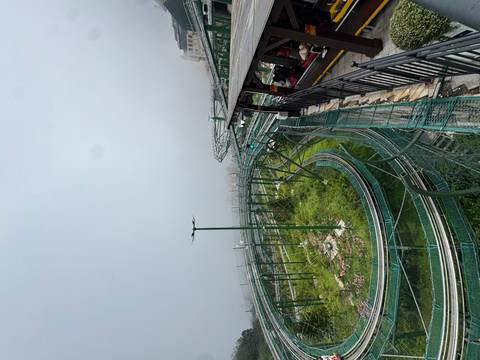 Spiralling alpine coaster track snakes through misty hillside amusement park