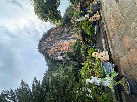 Limestone cliff rises above serene garden with statues and flowering plants