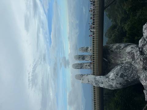 Massive stone hand supports pedestrian bridge high above forested mountains