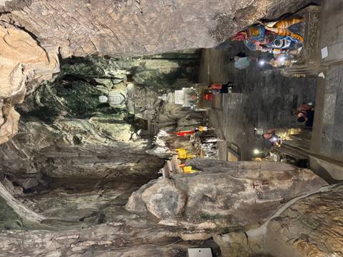 Dimly lit cave temple with large Buddha statue carved into rugged limestone chamber