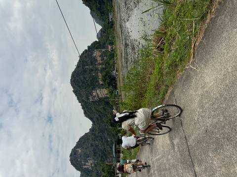 Cyclists ride along rural path beside wetland with karst hills in background