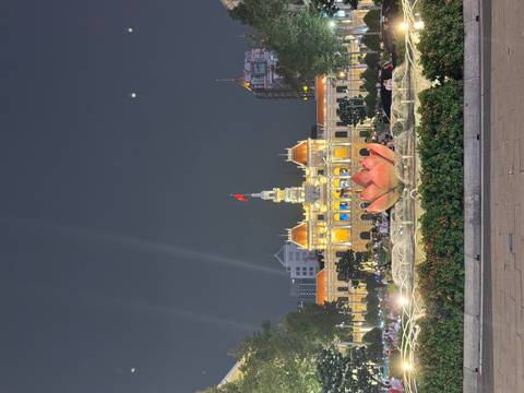Night view of the illuminated Ho Chi Minh City Hall behind a lotus-shaped fountain, with crowds enjoying the plaza.