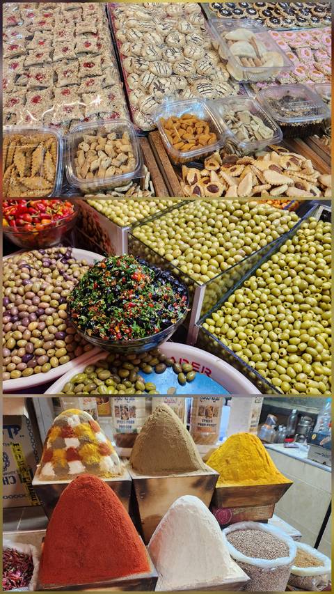 Vibrant market display of mixed olives and herbs in large bowls and bins.