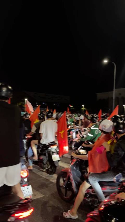 Crowded night-time street scene with dozens of motorbikes and Vietnamese flags during a lively celebration.