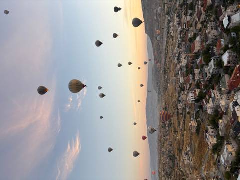 Dozens of colorful hot-air balloons drift over Cappadocia’s rocky landscape at sunrise.
