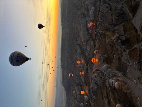 Long line of hot-air balloons illuminated pre-dawn over Cappadocia’s fairy-chimney terrain.