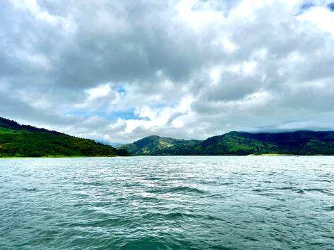 Expansive lake surrounded by rolling green hills under a dramatic cloudy sky.
