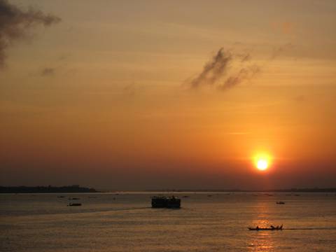 Orange sunset over a wide river with small boats silhouetted against the glowing sky.