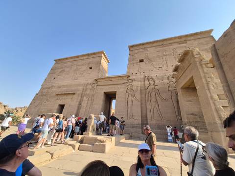 Crowd of tourists exploring the grand stone entrance of Philae Temple under a clear desert sky.