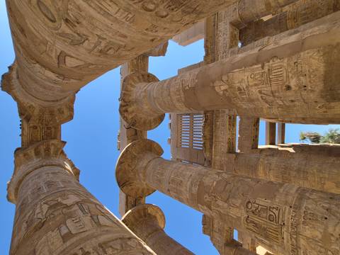 Upward perspective of massive hieroglyph-covered columns in Karnak Temple against deep blue sky.