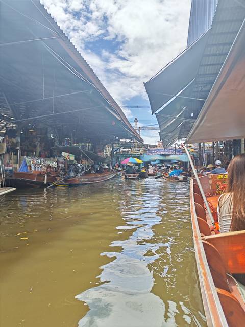 Bustling Thai floating market scene with many long-tail boats selling goods under a covered canal, colorful umbrellas and shoppers