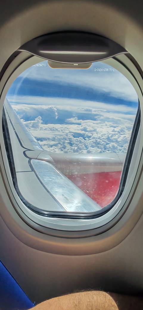 View from airplane window of wing and engine above dramatic cloudscape