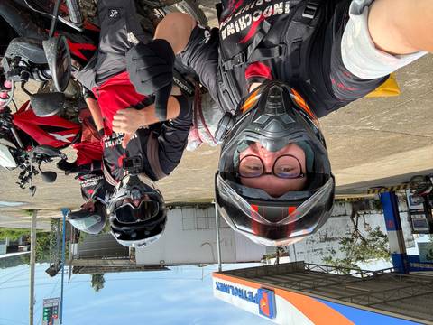 Motorbike riders taking cheerful selfie in gear and helmets, thumbs up at fuel station