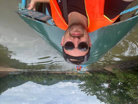 Selfie of traveller wearing lifevest and sunglasses on boat ride along calm river with karst hills in distance
