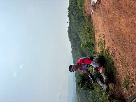 Tired rider seated on a red dirt track overlooking forested hills under a hazy sky