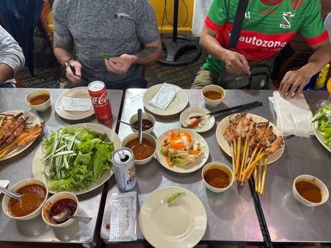 Vietnamese dinner spread with grilled skewers, fresh herbs and dipping sauces as diners reach in
