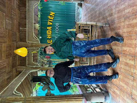 Two riders grinning in makeshift rain pants inside a bamboo-decorated eatery