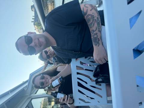 Casual candid of friends holding drinks on an open boat during daylight.