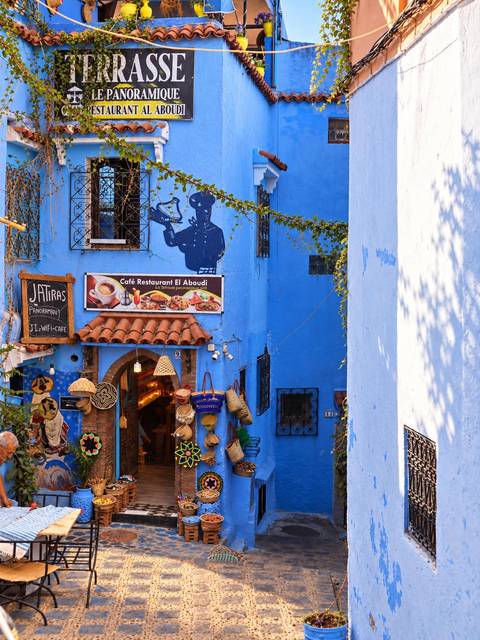 Blue-painted café façade in Chefchaouen with woven hats and local crafts on display.