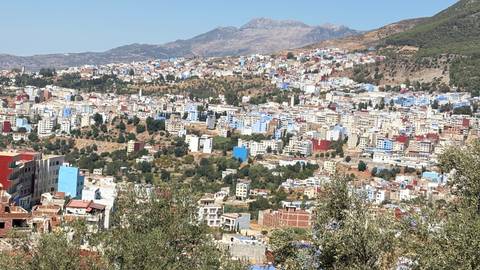 Expansive hillside view of Chefchaouen with clusters of blue and white buildings beneath mountains.