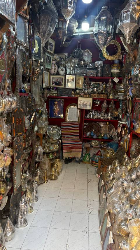 Crowded shop stall filled with intricate Moroccan metalware, ceramics and textiles displayed on shelves.